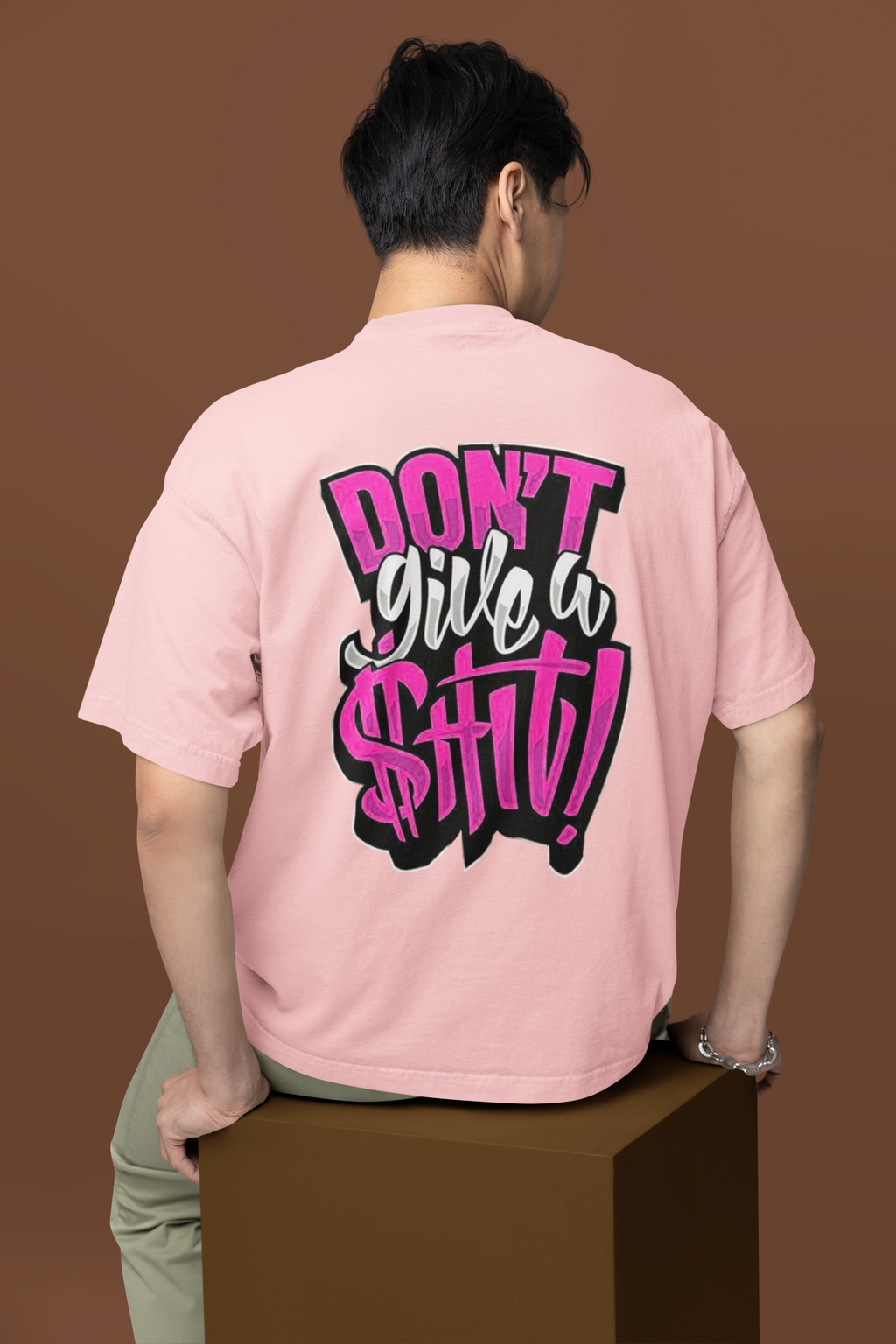 Person wearing a pink t-shirt with a graphic design on the back against a brown background