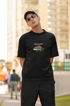 Man wearing a black oversized t-shirt with a sloth and “Energy Loading, Please Wait…” graphic, styled with black cap and sunglasses in an urban outdoor setting.