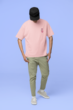 Full-body_view_of_a_man_standing_against_a_light_blue_background_looking_down_with_his_head_tilted_forward._He_is_wearing_a_light_pink_oversized_t-shirt_with_a_small_graphic_of_the_Pink panther