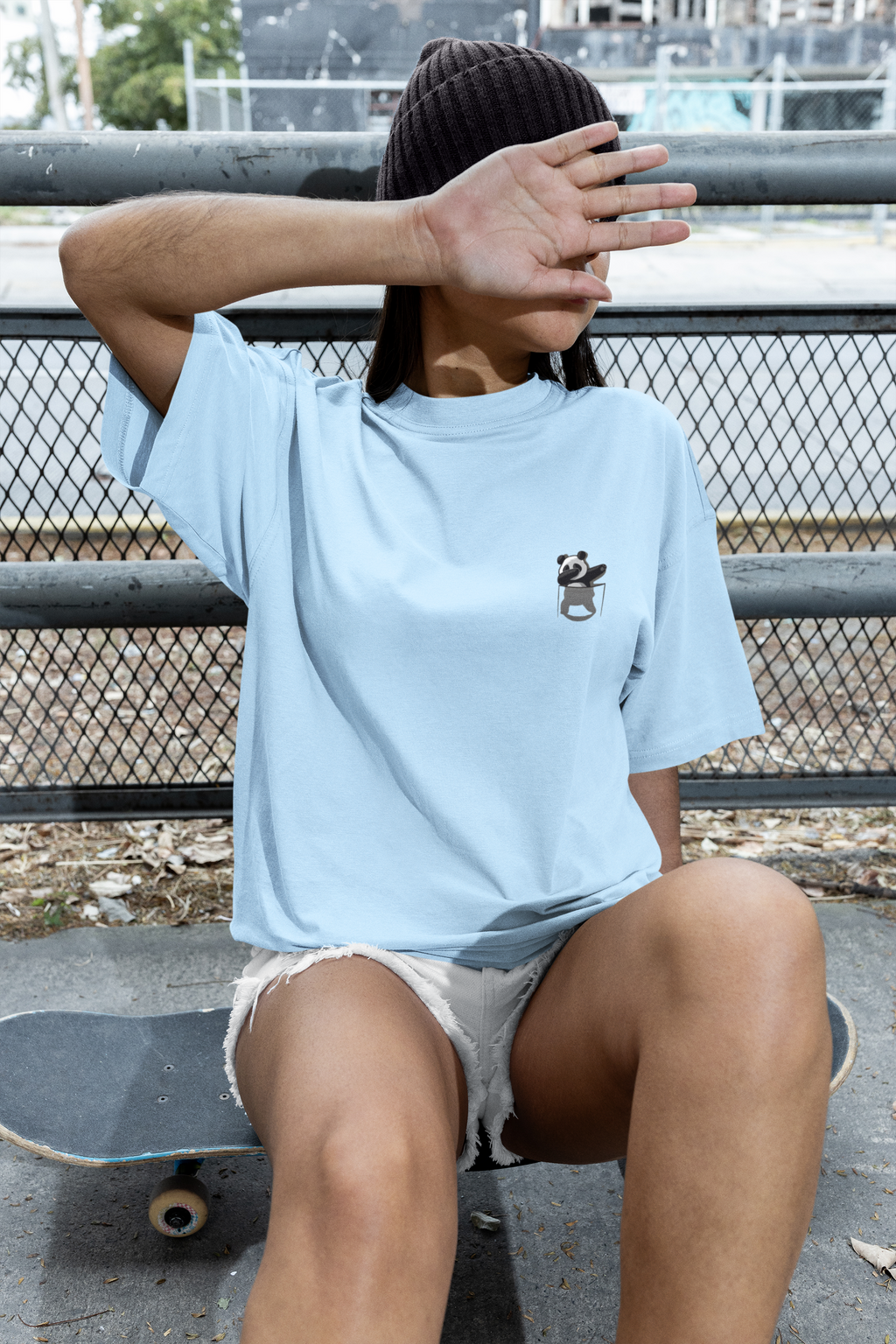 Person wearing a light blue t-shirt with a panda design, sitting on a skateboard.