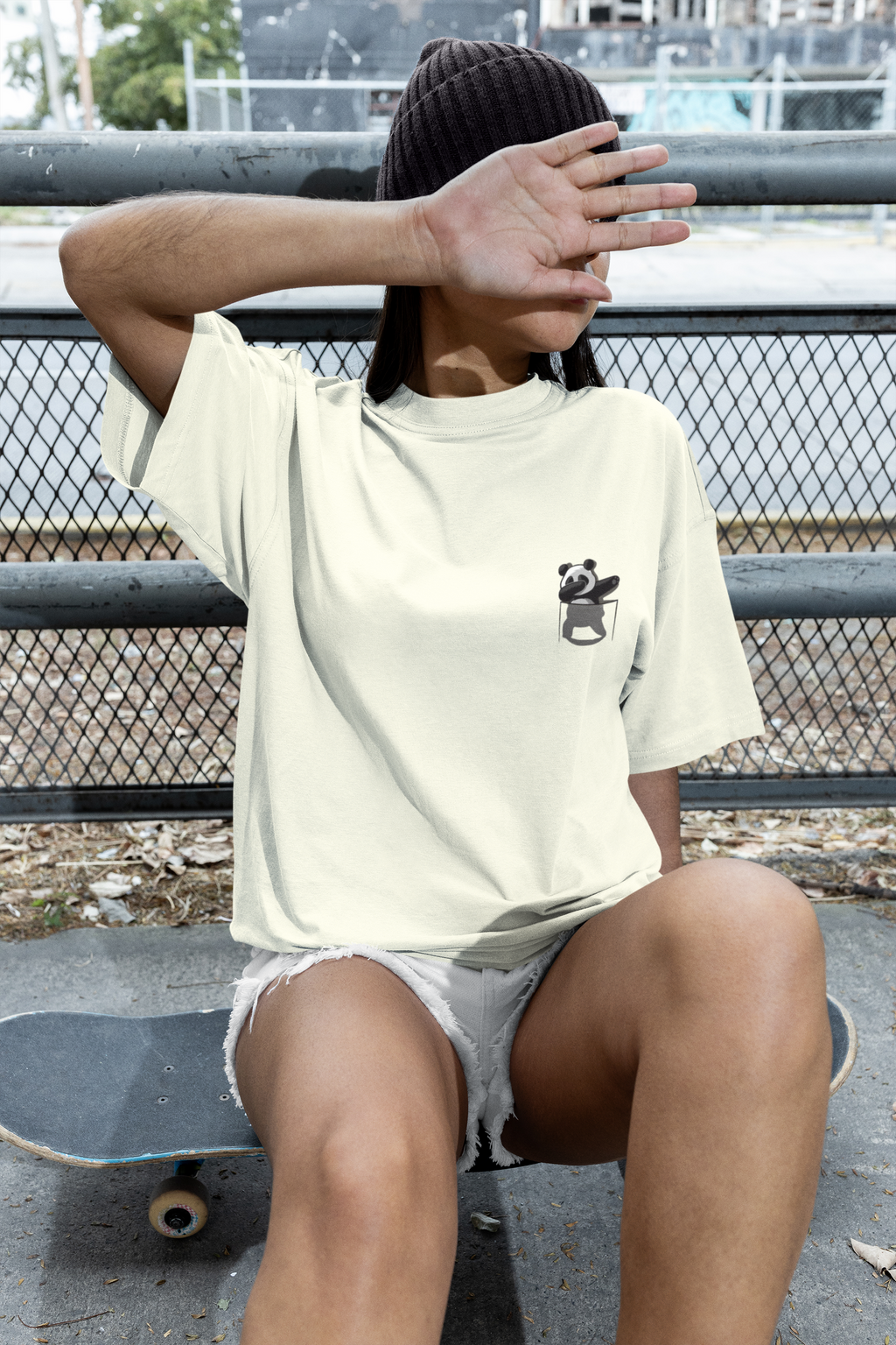 Person wearing a light-colored t-shirt with a panda design, sitting on a skateboard.